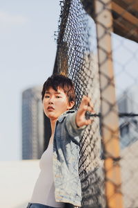 Portrait of young man standing against fence