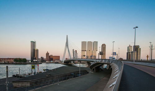 Erasmusbrug bridge over river by city against clear blue sky