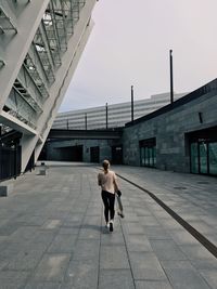 Rear view of woman with skateboard walking on footpath