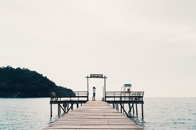 Side view of girl standing on pier over lake against clear sky