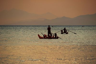 Men in boat on sea against sky during sunset