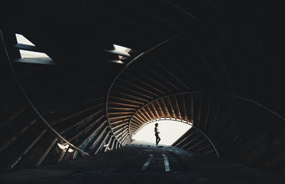 Side view of distant unrecognizable person standing at entrance in spacious round dark tunnel with metal rails and creative design person