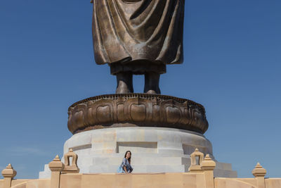 Woman standing by idol against clear blue sky