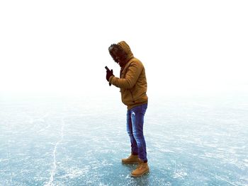 Side view of man holding smart phone while standing on frozen lake
