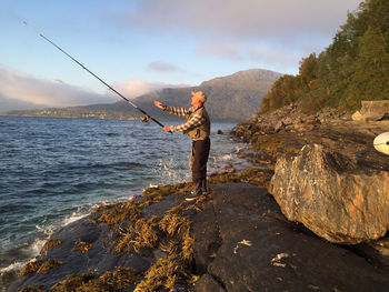 Side view full length of man fishing while standing at beach