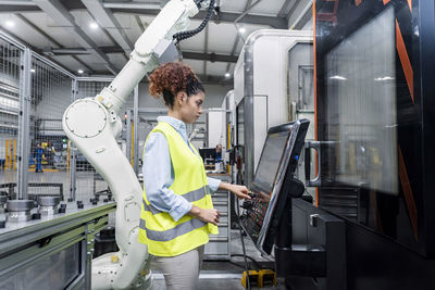 Engineer standing by robotic arm and operating machine in factory