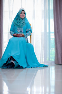 Full length of bride in traditional clothing sitting against window