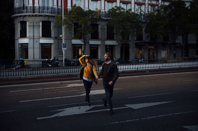 Husband and wife holding hand while crossing road in city