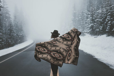 Rear view of woman with scarf standing on road in forest during foggy weather