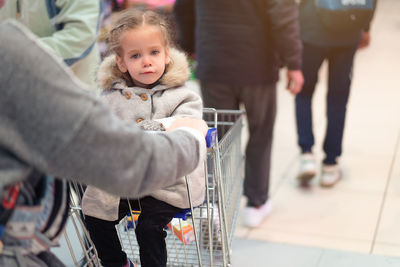 Portrait of girl sitting on shopping cart at supermarket