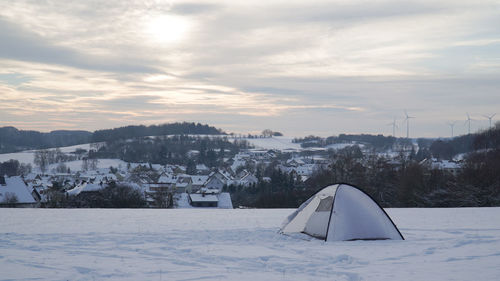 Snow covered field by buildings against sky