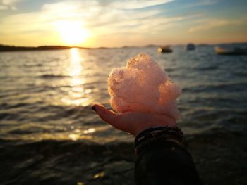 Cropped hand of woman with soap sud at beach against sky during sunset