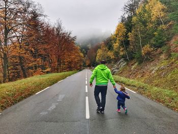 Rear view of father and daughter walking on road amidst trees during autumn