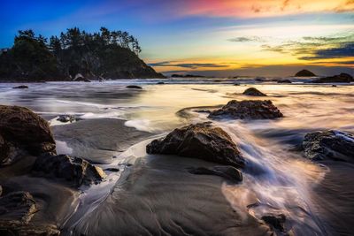 Rocks at sea shore against sky during sunset