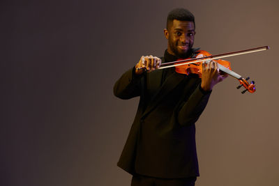 Young man holding violin against wall