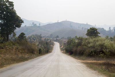 Country road along trees and mountains against sky