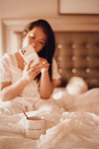 Woman holding mobile phone while relaxing on bed at home