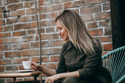 Woman holding coffee cup against brick wall