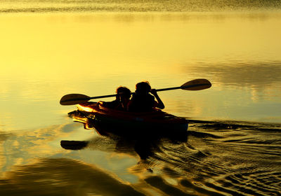 High angle view of silhouette boys canoeing on lake during sunset