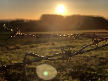 Barbed wire fence on field against sky during sunset