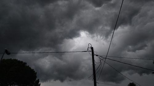 Low angle view of bird perching on cable against cloudy sky