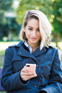 Portrait of smiling man holding smart phone at park