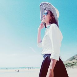 Low angle view of young woman standing at beach against sky