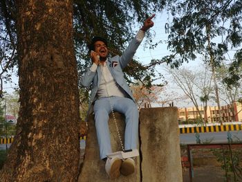 Man screaming on telephone while sitting by tree