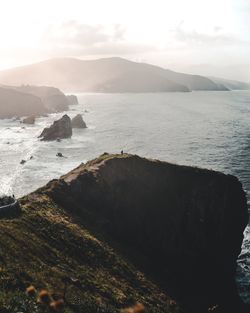 Scenic view of sea and rocky coastline with mountain against sky