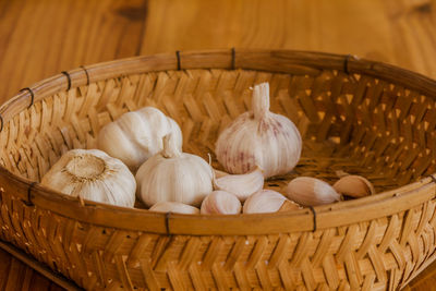 Dried garlic is placed in a wicker basket placed on a wooden floor.