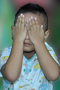 Close-up of boy covering face with two hands