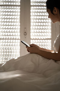 Woman using phone while sitting on bed at home