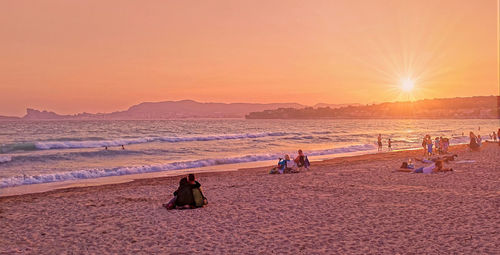 People on beach against sky during sunset