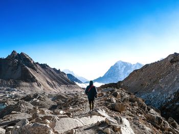 Rear view of man walking on mountain against clear blue sky