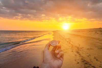 First person view of a man's hand with a compass against the backdrop of a beautiful seascape