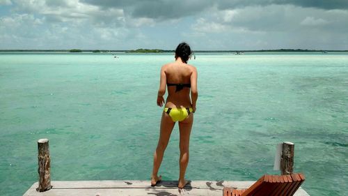 Rear view full length of sensuous woman in bikini standing on pier at beach