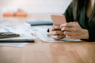 Midsection of woman using smart phone on table