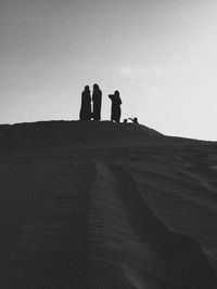 Silhouette people on desert against clear sky