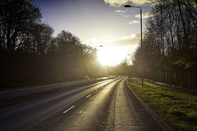 Road by trees against sky during sunset in city