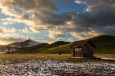 House on field by houses against sky during sunset