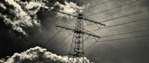 Low angle view of electricity pylon against cloudy sky