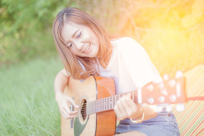 Young woman playing guitar on grassy field at park