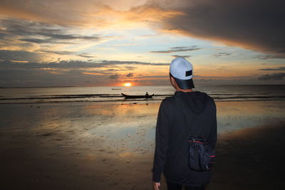 Rear view of man standing at beach during sunset