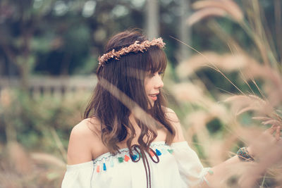 Smiling young woman wearing wreath touching plants on field
