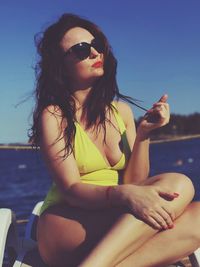 Young woman sitting in sunglasses against sea