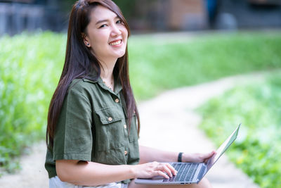 Young woman using mobile phone while sitting on field