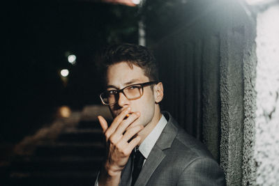 Portrait of businessman smoking cigarette by illuminated wall at night