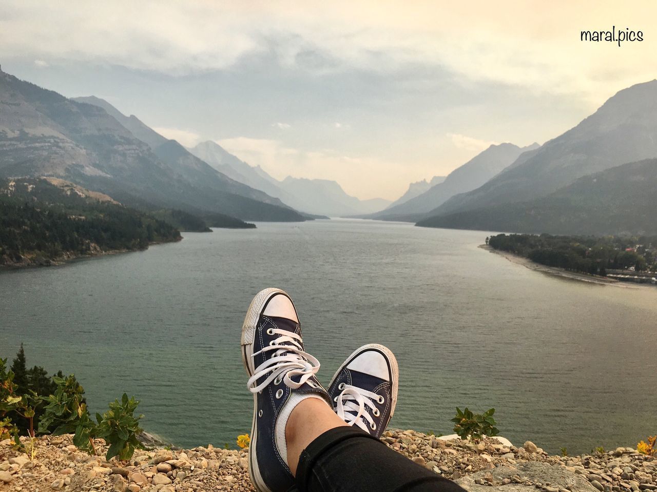 LOW SECTION OF PERSON STANDING ON LAKE BY MOUNTAIN