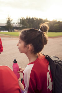 Side view of girl sitting by friends against soccer field