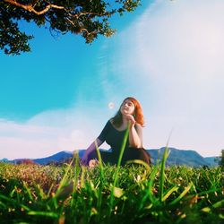 Low angle view of woman sitting on grassy land against sky